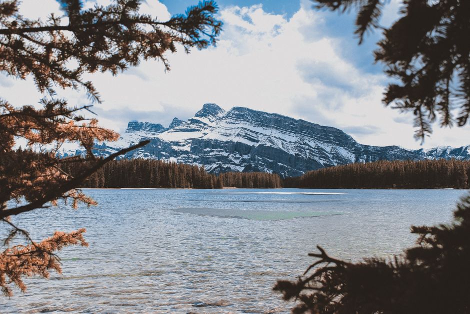 Breathtaking view of snowy mountains and clear lake framed by trees in Banff, Alberta.