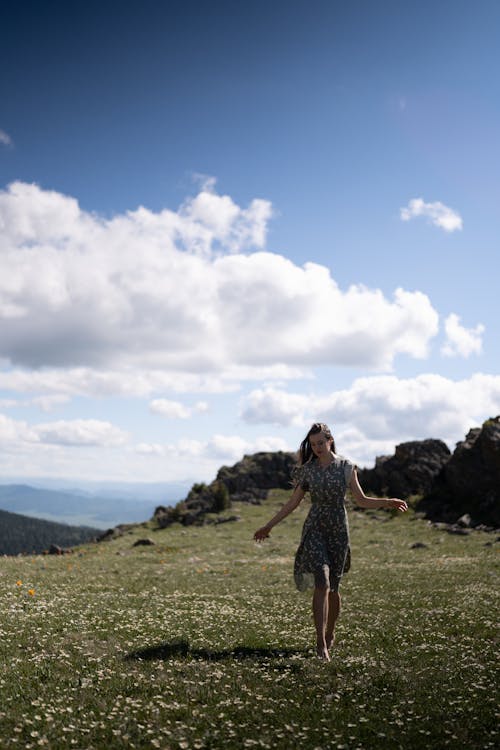 Photo of a Woman Walking on a Field with Grass and Flowers