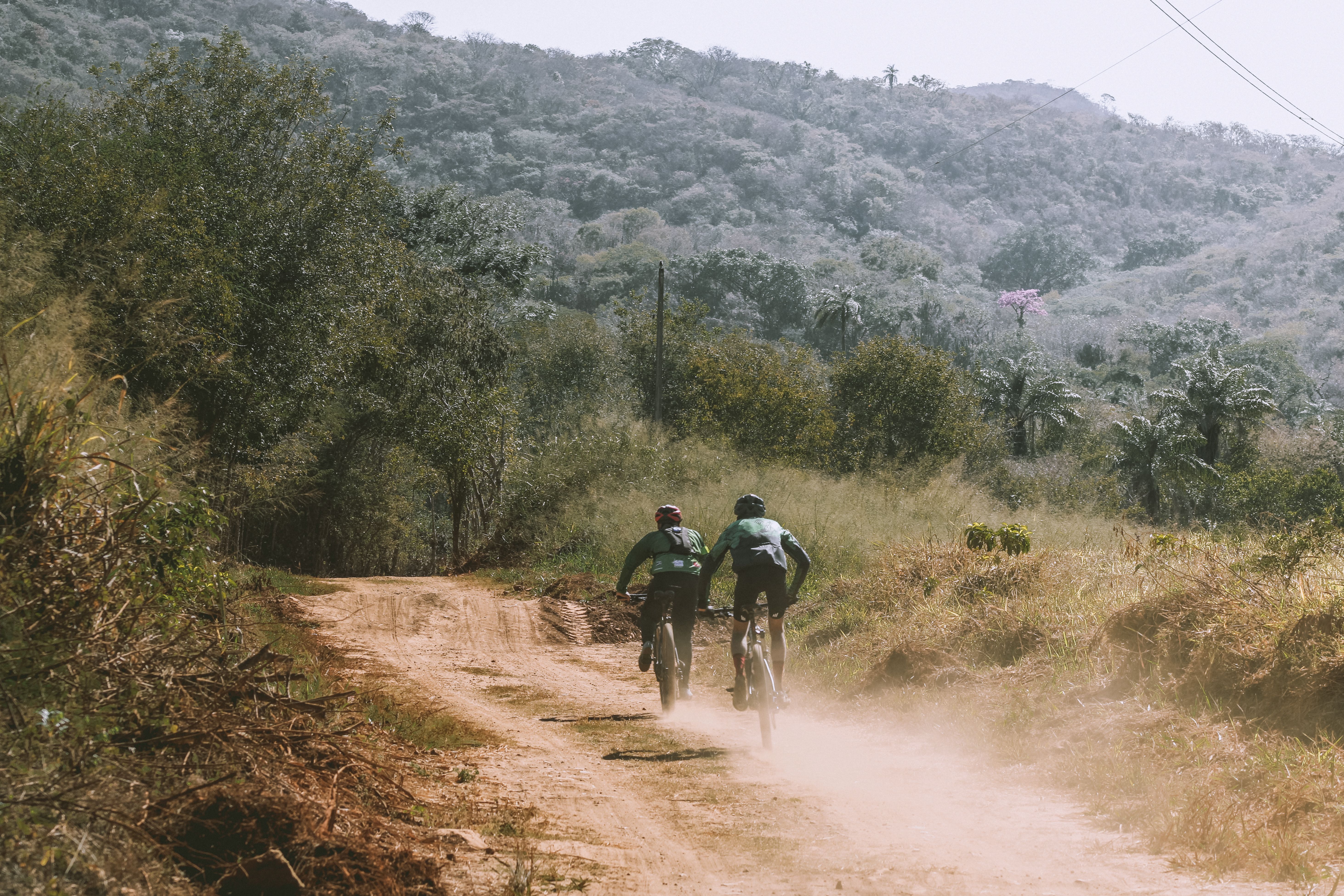 Dois ciclistas pedalando lado a lado conversando em estrada de terra