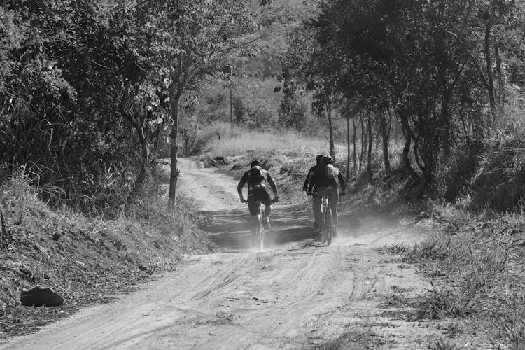 Grayscale Photo Of People Biking On A Dirt Road