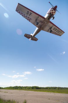 A vintage aircraft flying low above a runway under a clear blue sky.
