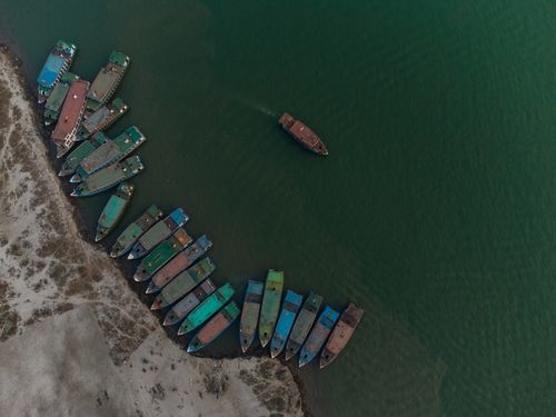 Free Birds-eye view of multiple sea vessels docked at a port, one ship sailing. Stock Photo
