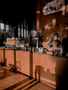 Barista in a stylish café prepares coffee, showcasing espresso machine and warm interior design.