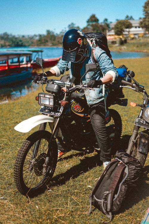 Free A biker in a denim jacket equips his motorcycle near a serene lakeside. Stock Photo