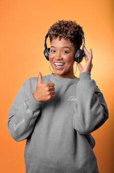 Cheerful woman wearing headphones giving a thumbs up against an orange background