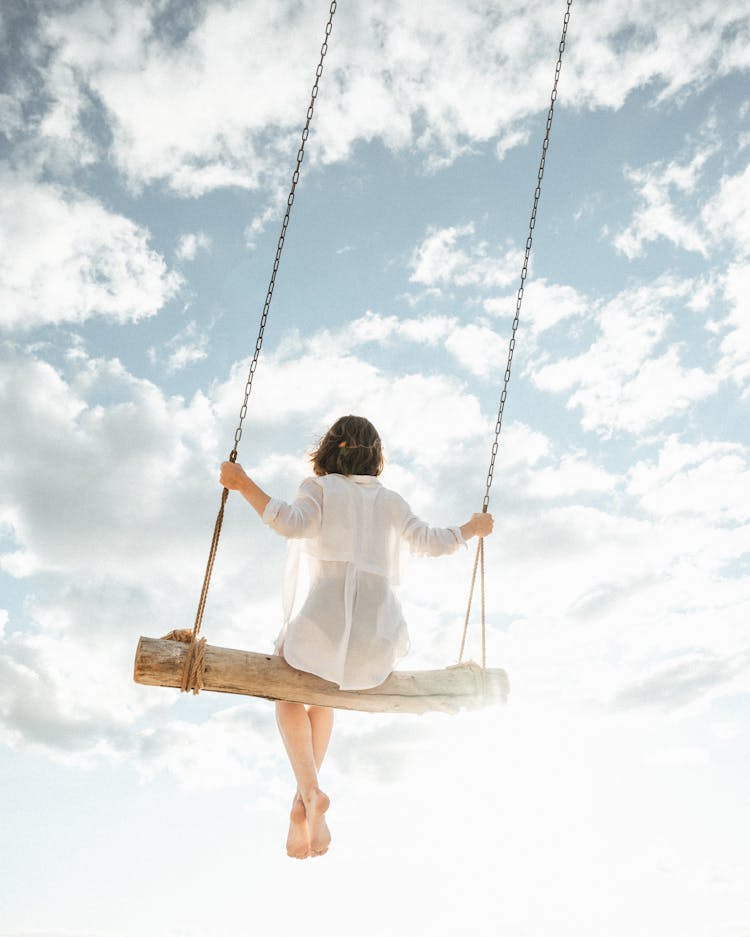 A Woman In White Dress Sitting On Swing