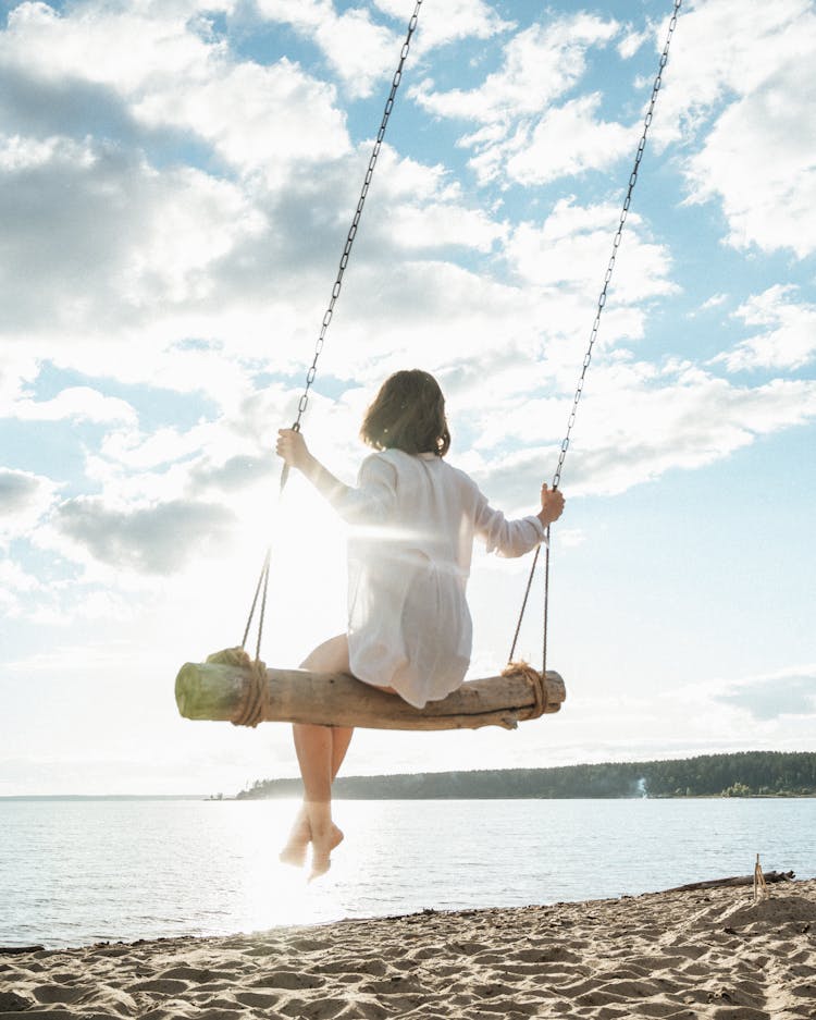 A Woman In White Long Sleeves Sitting On The Swing