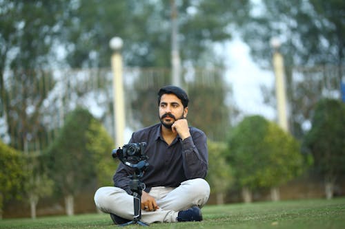 Man in Black Long Sleeves Sitting on Grass Near Camera 