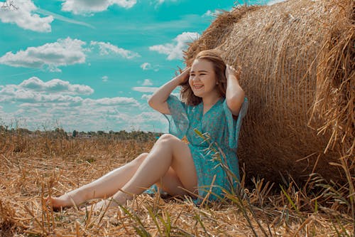 Woman in a Blue Dress Sitting in Front of Hay