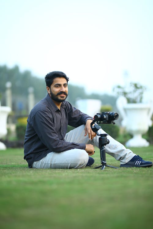 Smiling Man Sitting Beside a Camera on Grass