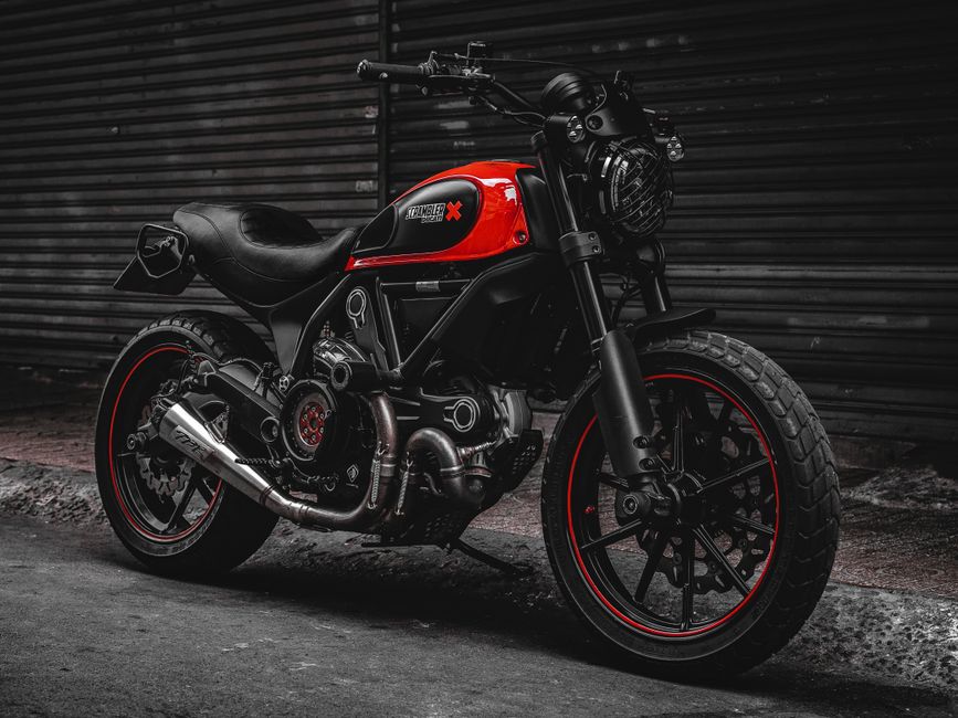 A stylish black and red Ducati Scrambler motorcycle parked on a city street, showcasing its robust design.