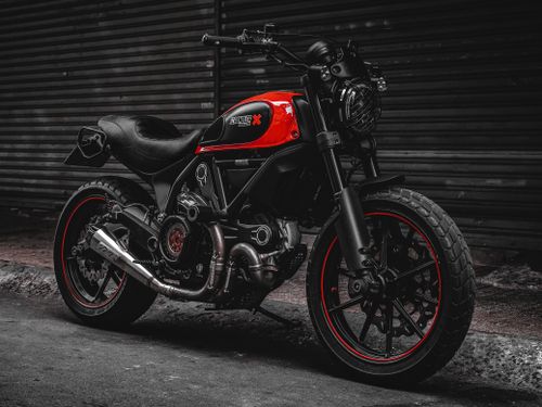 Free A stylish black and red Ducati Scrambler motorcycle parked on a city street, showcasing its robust design. Stock Photo