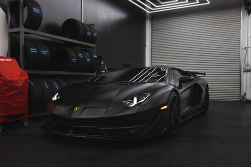 Free Luxury black Lamborghini in a contemporary garage setting with wheels and tools. Stock Photo