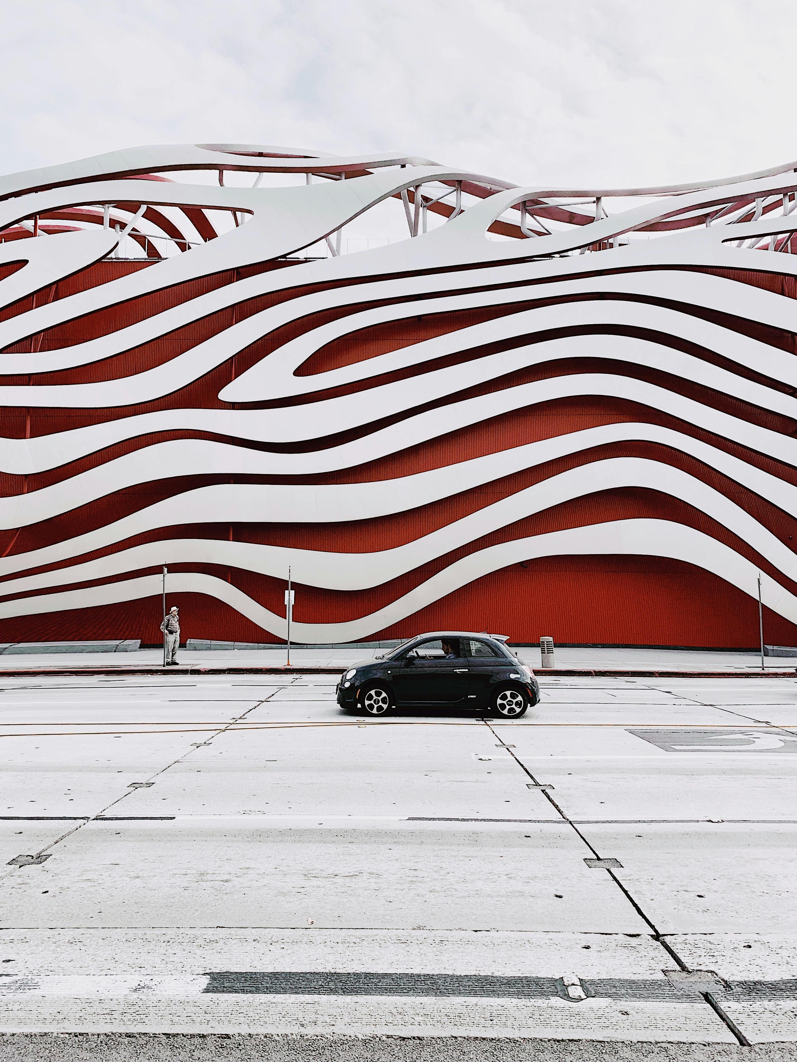 Black car in front of wavy red and white art museum facade.