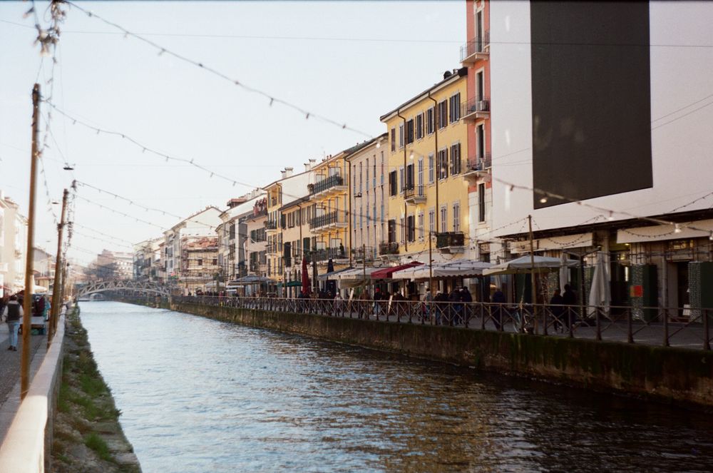 Stradă animată de-a lungul unui canal, cu magazine și ghirlande luminoase