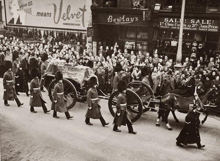 Grayscale Photo Of A Funeral Procession Accompanied By Soldiers On Street