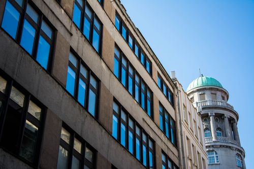 Free Contrast of modern building facade with historic dome under clear blue sky. Stock Photo