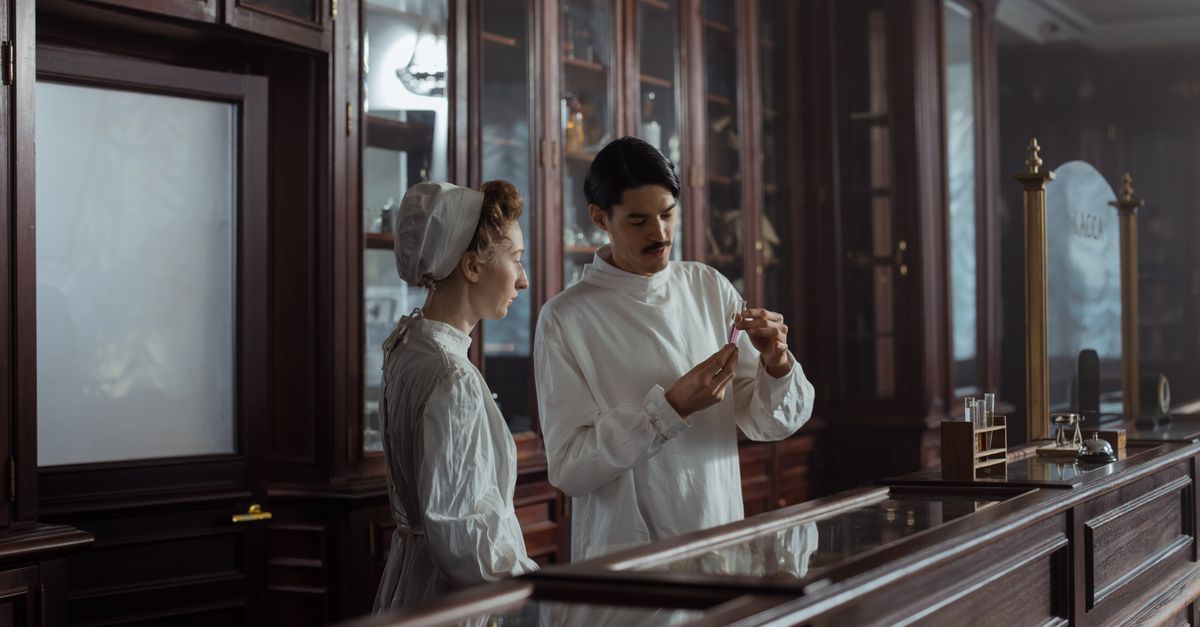 Two pharmacists in white gowns behind a pharmacy counter