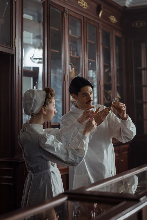 Free Retro scientist couple in vintage attire examining vials in an antique laboratory setting. Stock Photo