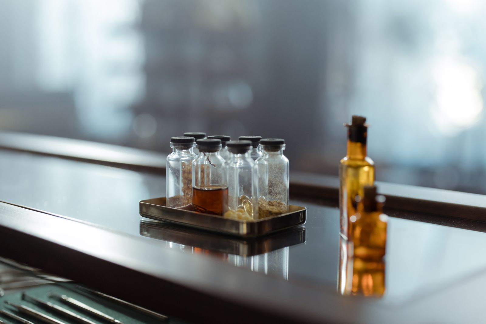 Small glass vials on a metal tray beside amber bottles on a reflective dark counter