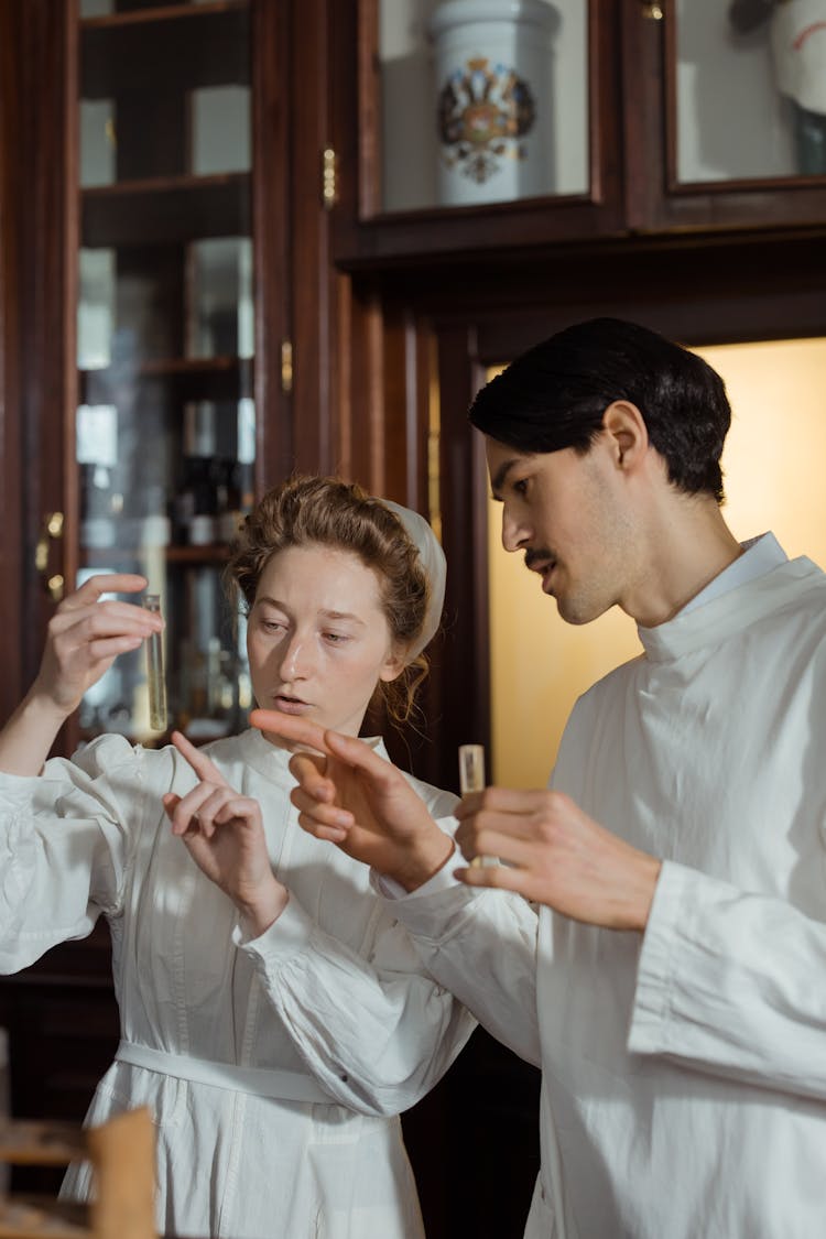 Nurses In White Long Sleeve Uniforms Holding And Looking At Test Tubes With Chemicals