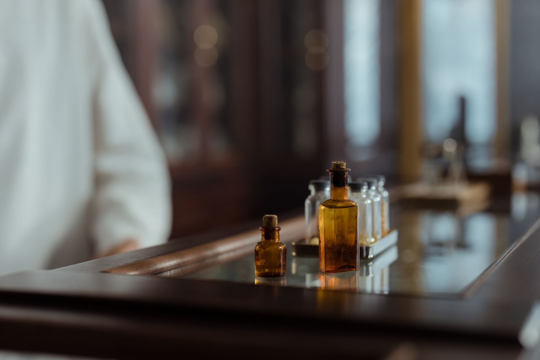 repurposed drug guide — A collection of vintage glass bottles displayed on a wooden table in an indoor setting.