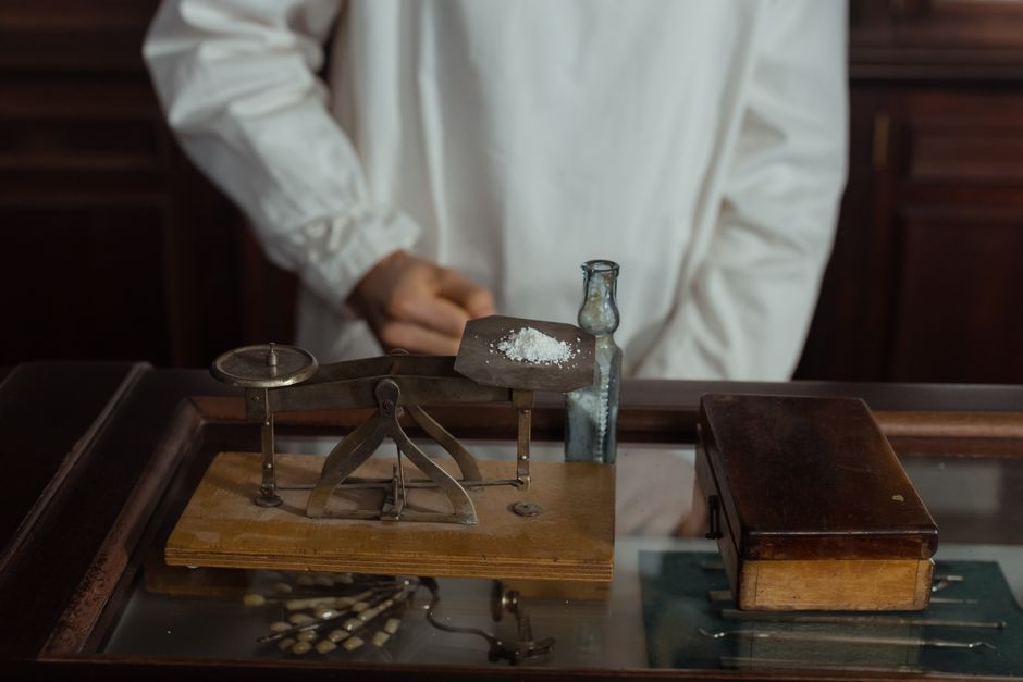 A pharmacist in a white gown working with a vintage scale and medicine bottle, showcasing retro pharmacology tools.