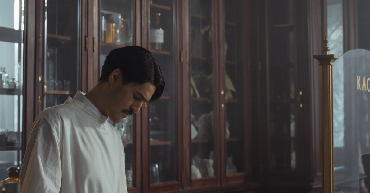 A pharmacist in a white gown behind a pharmacy counter