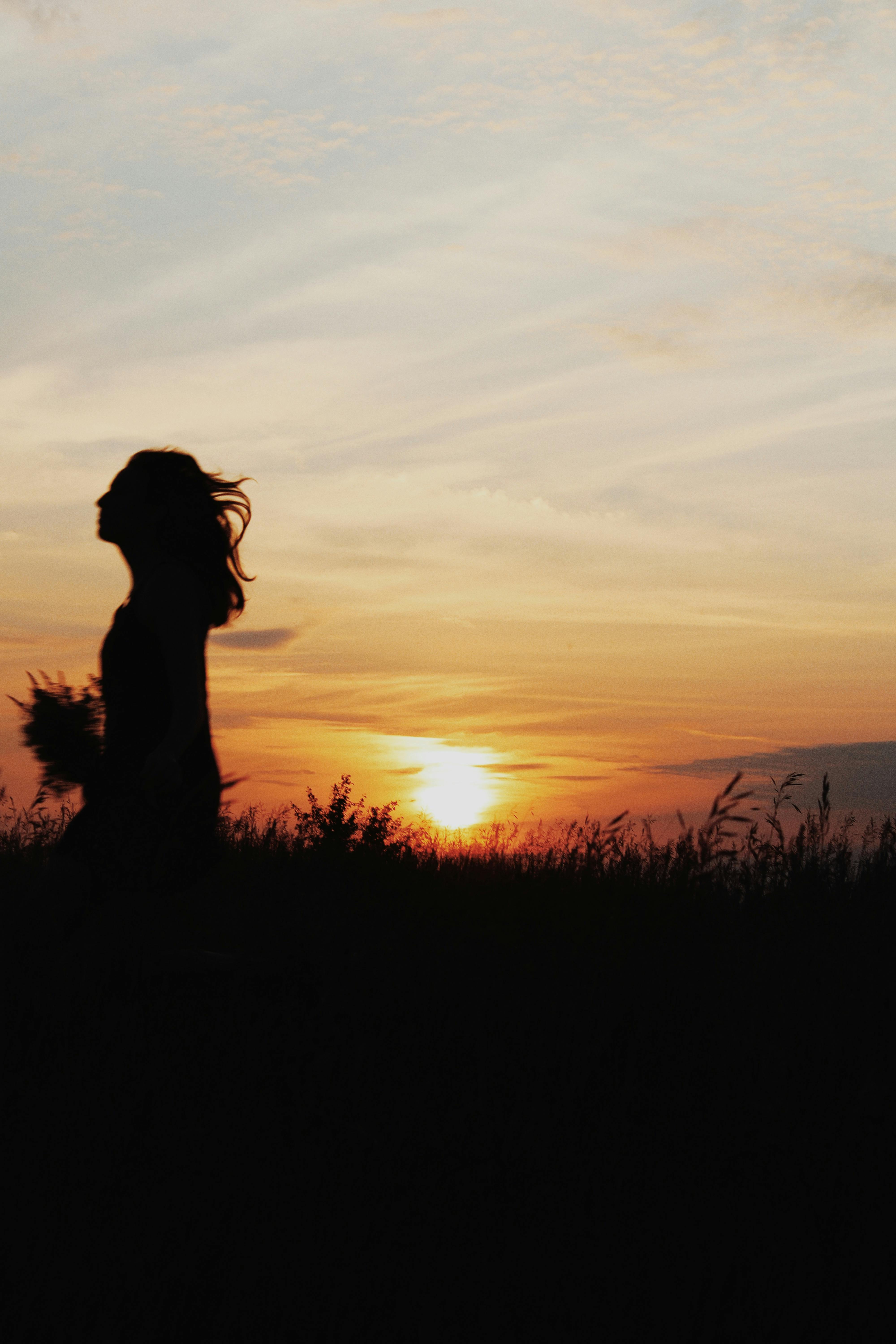 A woman walks in a field during sunset, capturing her silhouette against the golden sky.