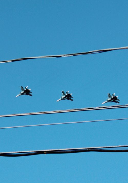 Free Three fighter jets soar in formation above electric wires on a clear day. Stock Photo