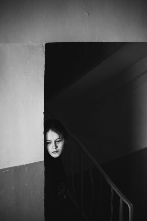 Free A woman in a dim hallway, leaning against a concrete wall with a sad expression. Stock Photo