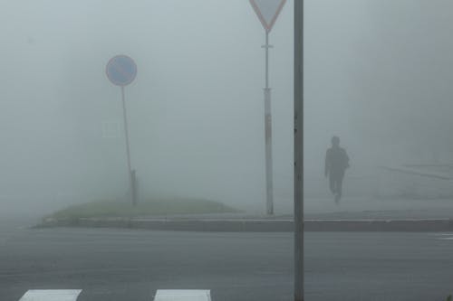 Photo of a Person Walking on a Street During a Foggy Day