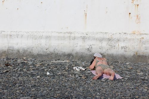 Free A woman sunbathes on a pebble beach beside a concrete wall, enjoying a summer day. Stock Photo