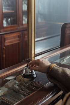 A hand ringing a call bell on a vintage wooden counter in a classic setting, emphasizing nostalgia.