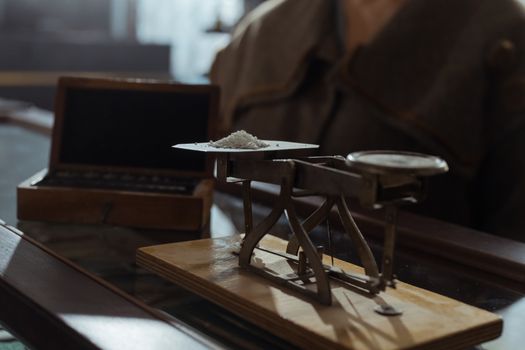 Classic vintage weighing scale with a small heap of white powder placed indoors on a wooden surface.