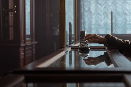 Free A hand pressing a service bell on an elegant wooden hotel desk, creating a classic atmosphere. Stock Photo