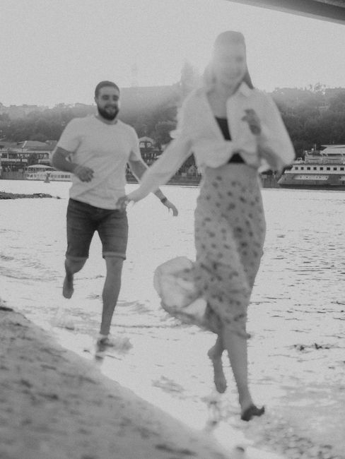 A romantic black-and-white photo of a couple joyfully running along a beach.