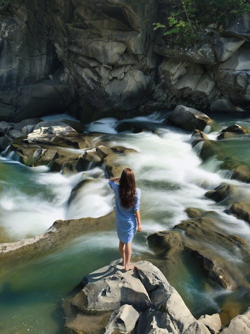 Frau Im Blauen Langärmeligen Kleid, Das In Der Mitte Des Felsens Mit Tobendem Wasser Steht