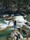一名妇女站在岩石上，欣赏着自然环境中风景优美的河流