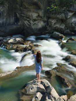 一名妇女站在岩石上，欣赏着自然环境中风景优美的河流