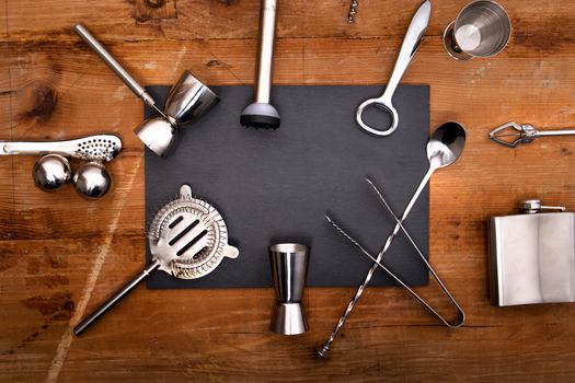 Flatlay of essential stainless steel bar tools arranged on a wooden surface for cocktail making.
