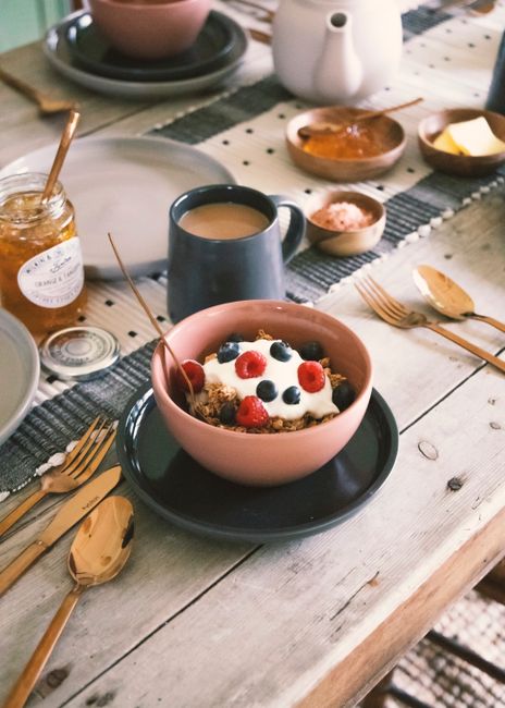 A cozy breakfast scene featuring yogurt with berries, tea, and honey on a rustic table.