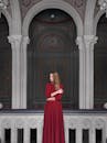 一位身穿红色连衣裙的女子站在宏伟的拱门与柱子之间，展示着经典建筑之美