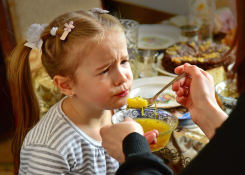 A mother feeding her young daughter soup indoors, showcasing family care.