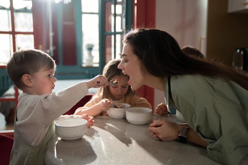 Free A mother enjoys a playful breakfast moment with her children, sharing quality family time indoors. Stock Photo