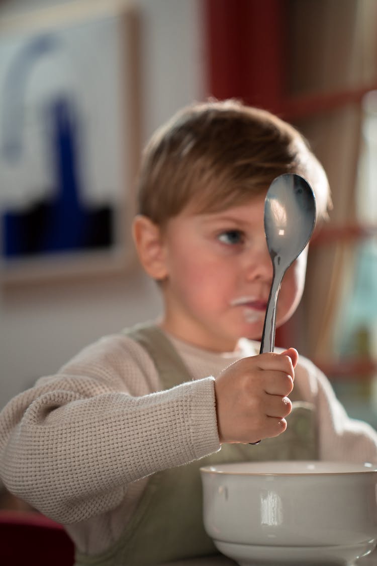 Child In White Sweater Holding Silver Spoon