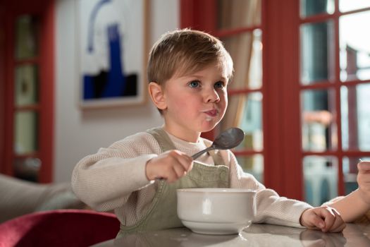 A young boy happily eating breakfast inside a cozy room, capturing a warm family moment.