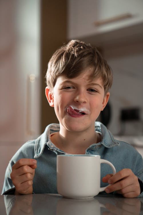 Free Boy in Blue Denim Shirt Holding a Cup of Milk with Tongue Out Stock Photo