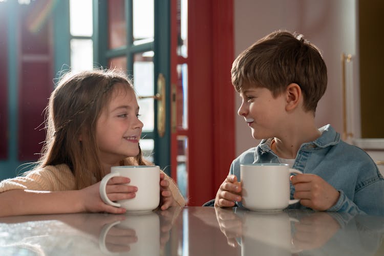 Two Kids Looking At Each Other While Holding Cup Of Milk