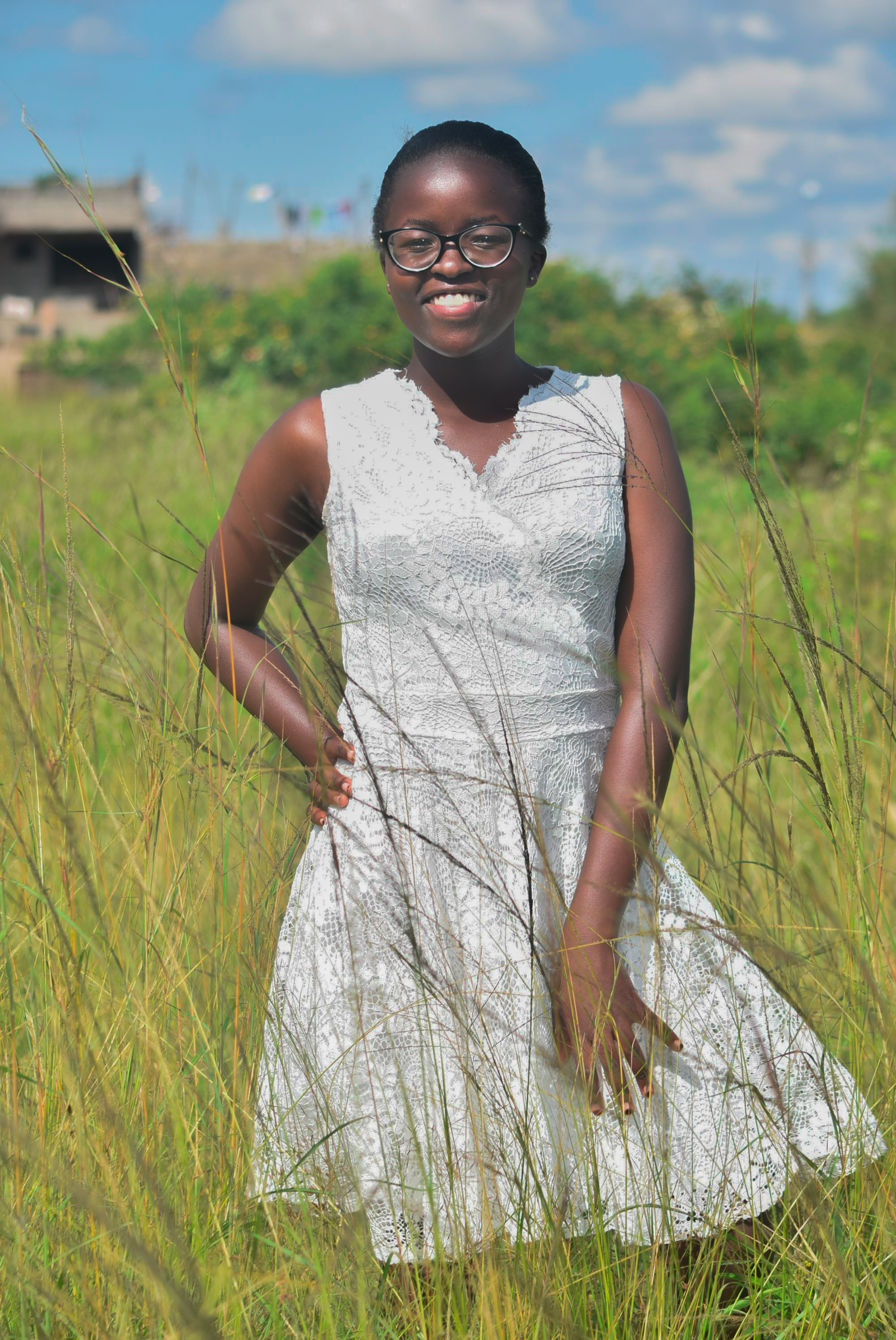 A joyful woman in a white dress poses in a sunlit field, exuding happiness.